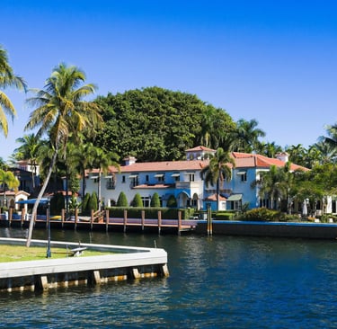 Luxury waterfront mansion in Miami with palm trees, a private dock, and Mediterranean architecture.