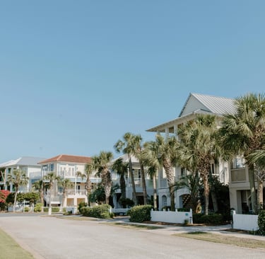 Luxury beach vacation rentals and palm trees along a quiet coastal street under a clear blue sky.