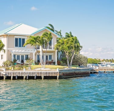 Luxury waterfront tropical villa with palm trees and a private boat dock on blue water.