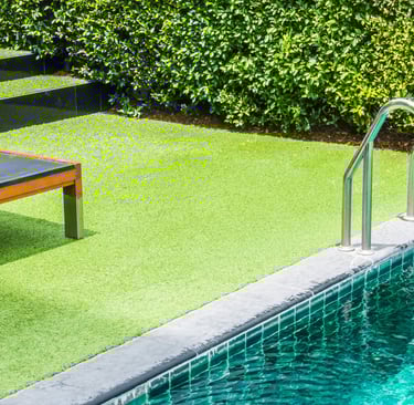 Luxury swimming pool with artificial grass turf, a wooden sun lounger, and stainless steel handrails.