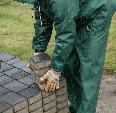 Worker in green rain gear stacking concrete paving stones for a patio landscaping project in the rain.