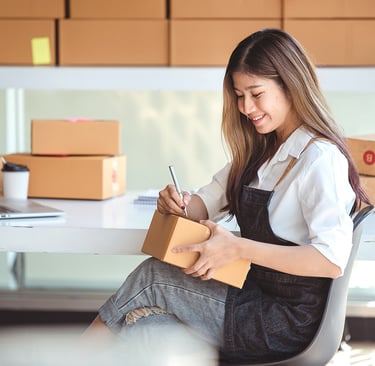 Smiling small business owner labeling cardboard shipping boxes for e-commerce order fulfillment.