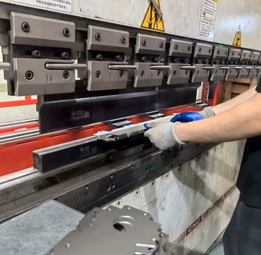 A metal worker uses a hydraulic CNC press brake machine to bend precision sheet metal parts.