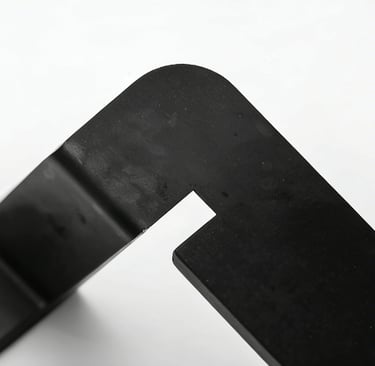 Close-up of a matte black metal furniture leg bracket with a rounded corner and industrial finish.