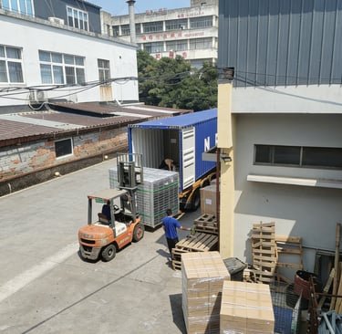 Forklift loading palletized boxes into a blue shipping container at an industrial warehouse dock.