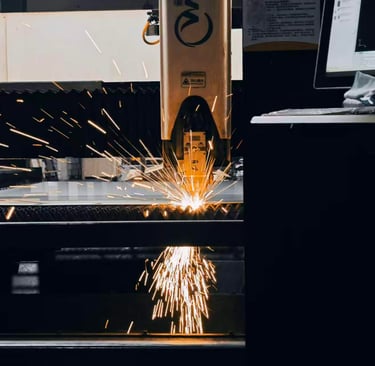 Industrial CNC fiber laser cutting machine processing a metal sheet with bright sparks in a factory.