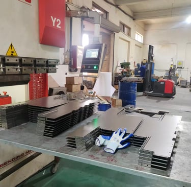 Precision sheet metal fabrication workshop featuring a CNC bending machine and stacked steel parts.