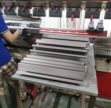 A factory worker operating a metal hydraulic press brake machine to bend steel sheets.