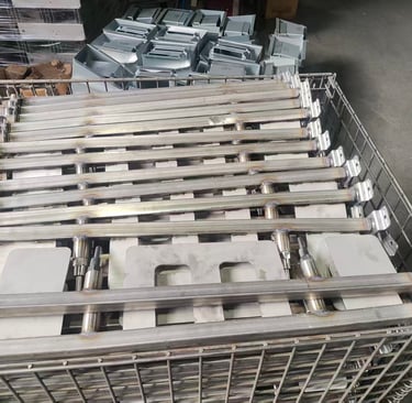 Stacked industrial stainless steel handrail components in a wire storage crate for manufacturing.