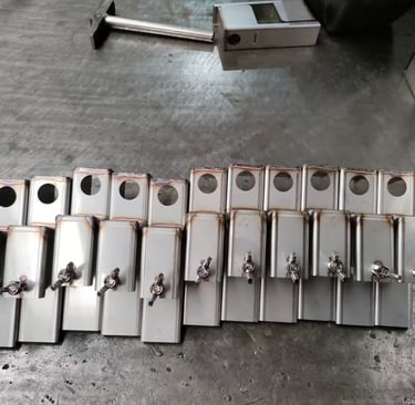 Custom fabricated stainless steel metal brackets with wing nuts on a factory workbench.