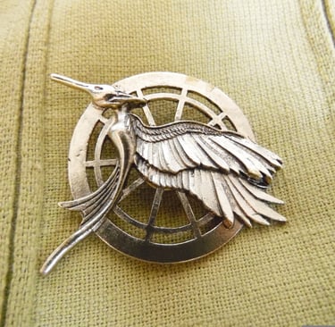 Resenha do livro Jogos Vorazes de Suzanne Collins: foto em close do broche do tordo.