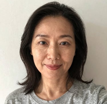 Smiling woman in workout gear holding a smoothie in a bright kitchen.
