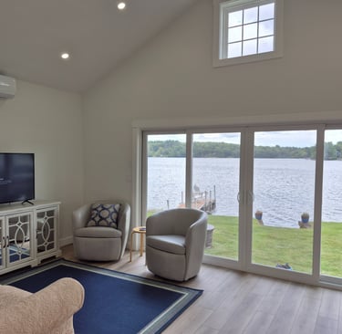 Modern lakefront living room featuring grey swivel chairs and a scenic waterfront view through sliding glass doors.