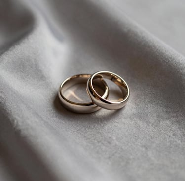 Detailed photography of a pair of high-end wedding rings resting on a warm grey silk fabric, soft morning light, minimalist and sophisticated composition, cream and taupe tones, Hispanic setting.