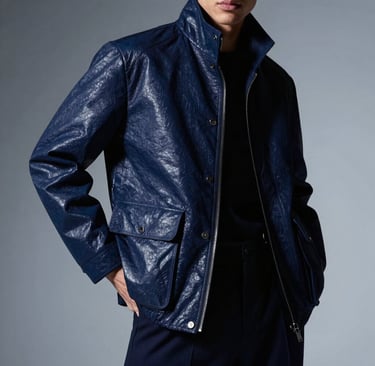 High-fashion editorial photography of a visionary artist in a North American / US studio. The subject wears a structured midnight blue jacket, standing in a powerful, confident pose. The lighting is dramatic and moody, with soft silver-blue highlights reflecting off the fabric. Immersive, sophisticated atmosphere.