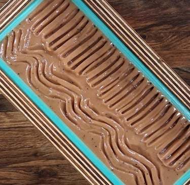 Freshly poured artisan soap batter with textured wavy patterns in a blue lined loaf mold.