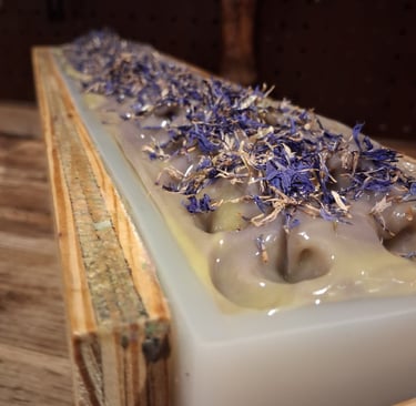 Handmade huckleberry soap loaf in a wooden mold topped with dried blue cornflower petals.