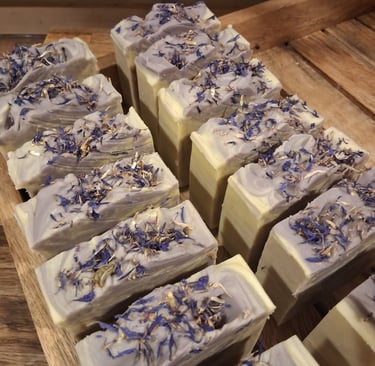 Handmade artisanal lavender soap bars topped with dried blue cornflowers on a wooden drying rack.