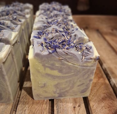 Handmade huckleberry artisan soap bars with dried botanical petals on a rustic wooden tray.
