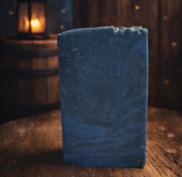 Handmade rustic blue bar soap on a wooden table with a lantern background.