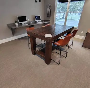 Picture of an office with two computer monitor and a table with four red chairs