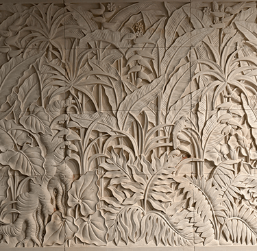 Hand-carved limestone wall relief featuring a lush tropical jungle scene with palm leaves and exotic birds.
