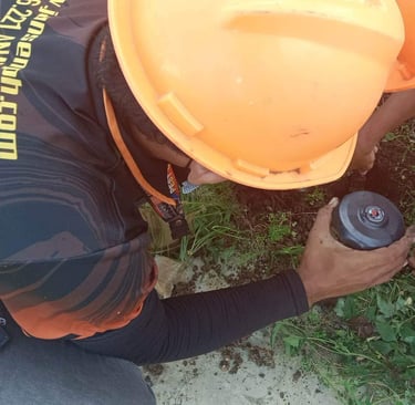 A pest control technician in a hard hat installs an underground termite bait station in soil.