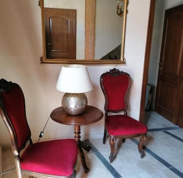 Antique red velvet chairs and a wooden side table with a lamp in a classic foyer with a large gold mirror.