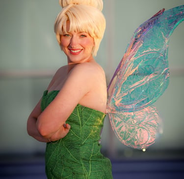 A fairy perfromer smiling featuring a green leaf dress and shimmering iridescent fairy wings.