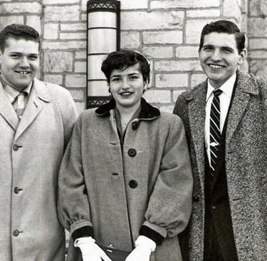 Vintage black and white photo of three young adults in formal coats and ties posing outdoors.