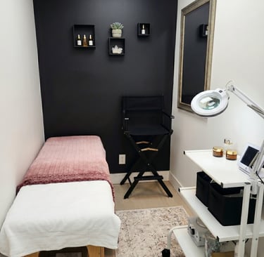 Modern aesthetician room with a facial treatment table, black accent wall, and professional skincare equipment.