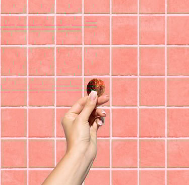 A hand holding a round piece of gummy against a pink tiled wall background.