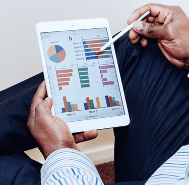 A businessman using a stylus to analyze financial data charts on a digital tablet.