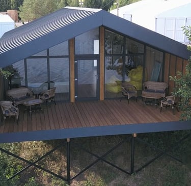 Modern black prefab cabin with glass walls and wooden deck on a metal foundation.