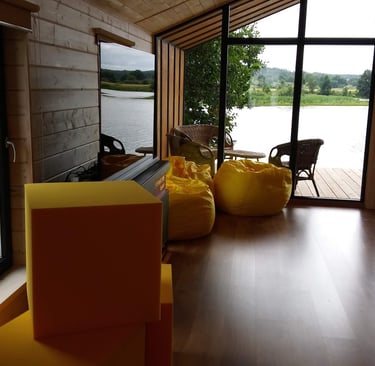 Modern log cabin interior featuring yellow bean bags and floor-to-ceiling windows overlooking a scenic lake.