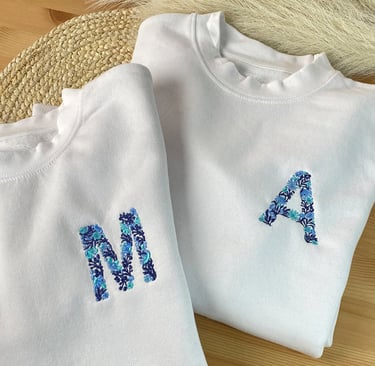 Two white custom sweatshirts with blue floral embroidery of initials M and A.