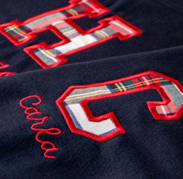 Close-up of a navy blue sweatshirt featuring red embroidered letters with plaid fabric inlay.