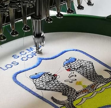 Industrial embroidery machine stitching a custom logo crest with blue and green thread.