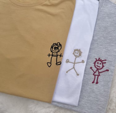 Custom embroidered t-shirts featuring personalized children's stick figure drawings in mustard, white, and grey.