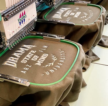 Tajima commercial embroidery machine stitching custom university logos on brown sweatshirts.