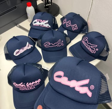 Navy blue Gambitas Morugas trucker hats featuring pink embroidered logos on a white table.