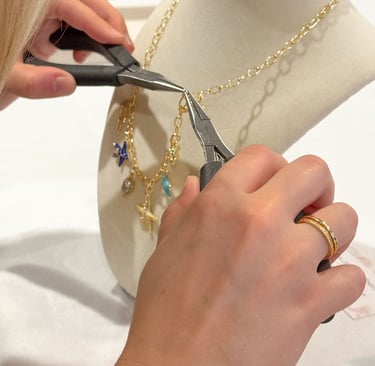 Artesana utilizando pinzas para colocar un dije en un collar de cadena dorada