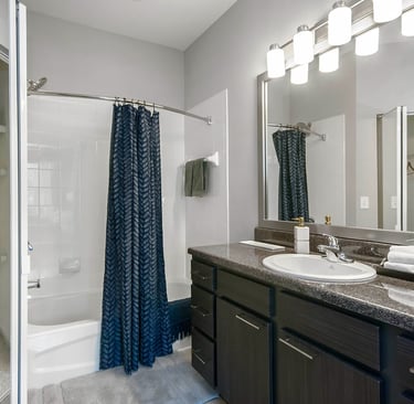 Modern bathroom featuring a dark wood vanity, granite countertop, and a shower with a blue patterned curtain.
