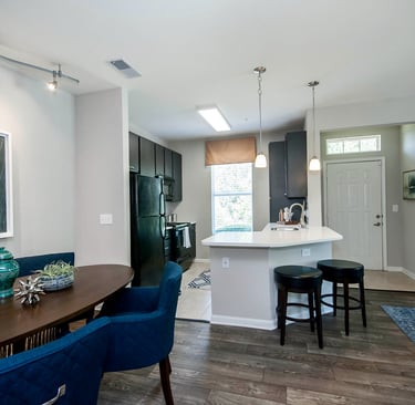 Modern open concept apartment interior featuring a dark wood dining table, blue chairs, and a kitchen with white counters.