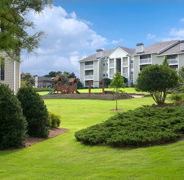 Suburban apartment complex featuring a wooden children's playground on a lush green lawn.