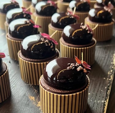 Gourmet dark chocolate mousse domes with mirror glaze and gold leaf garnish on striped pastry cups.