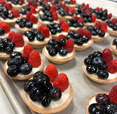 Mini fruit tarts with vanilla cream, fresh blueberries, and raspberries on a baking sheet.