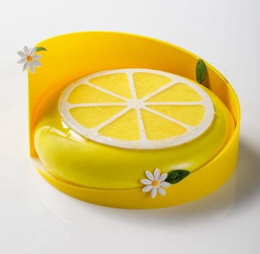 Gourmet lemon mousse cake with a yellow mirror glaze, citrus slice topper, and white fondant daisies.