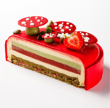 Gourmet layered strawberry pistachio mousse cake with red mirror glaze and mushroom decorations.