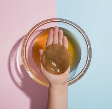 Una mano sosteniendo un SCOBY orgánico de kombucha sobre un recipiente de vidrio con líquido iniciad